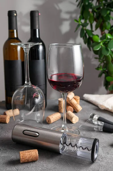 Elektrikli gri metal tirbuşon, havalandırma ve şarap için elektrikli süpürge. Gri beton arka planda. Arka planda iki şişe şarap ve bardak var..