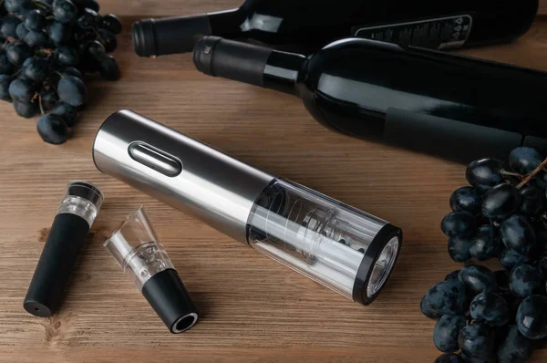 Electronic cordless corkscrew metallic. On a wooden background. Near the aerator and the vacuum stopper for the bottle. In the background grapes  and a bottle of wine.