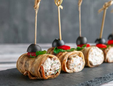 Peynir ve otlarla doldurulmuş kızarmış patlıcan kanapeleri. Tatlı biber, maydanoz ve zeytinle süslenmiş. Siyah bir tahta üzerinde. Gri arka plan. Yakın plan..