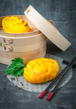 Bambu kazanda buğulanmış boya çöreği. Maydanoz ve baharatla süslenmiş pirinç kağıdının üzerinde yatıyordu. Çubukların yanında. Arka planda bambu kazanı var. Gri arka plan. Geleneksel Kore sokak yemekleri.