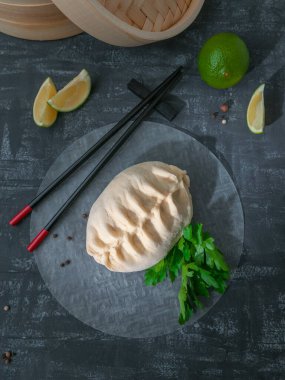 Pyans çöreği buğulandı. Tavuk, havuç ve lahanayla dolu. Arka planda bambu kazan, limon, acı biber ve soya sosu var. Yukarıdan bak. Gri arka plan. Geleneksel Kore sokak yemekleri.