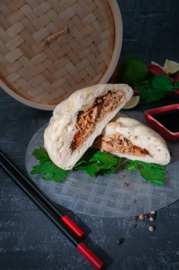 Pyans çöreği buğulandı. Domuz eti, mantar ve soğanla kaplı. Bir kaşığı pirinç kağıdına yarıya böl. Baharat ve maydanozla servis edilir. Arka planda bambu kazan, limon, acı biber ve soya sosu var. Yakın plan. Geleneksel Kore yemekleri.