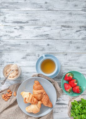 Kahvaltıda. Bir fincan çay, taze kruvasan, mis kokulu çilek ve hindistan cevizi ezmesiyle. Gri ahşap arka planda kompozisyon. Mesaj için yer. Düz yatıyordu. Dikey resim.