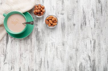 Gri ahşap bir masada kremalı yeşil fincan çay. Bir peçete ve fındık ve bademlerle dolu kâselerin yanında. Mesaj için yer. Düz yatıyordu. Yukarıdan görüntüle.