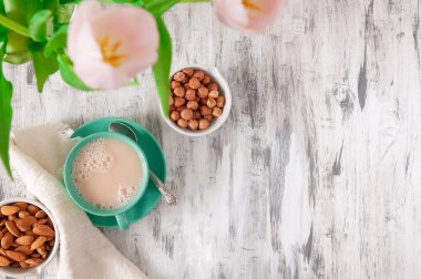 Gri ahşap bir masada kremalı yeşil fincan çay. Bir peçete ve fındık ve bademlerle dolu kâselerin yanında. Mesaj için yer. Düz yatıyordu. Yukarıdan görüntüle.