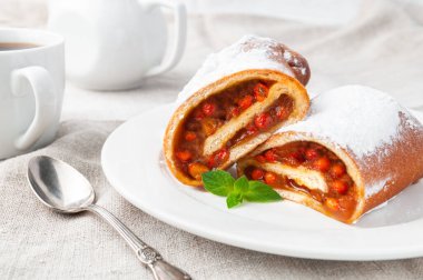 Dondurulmuş şeker serpiştirilmiş hamur hamurundan yapılmış deniz dikenli tatlı rulo. İkiye böl. Beyaz bir tabakta yatıyor. Bir tutam nane ile süslenmiş. Ev yapımı. Arka planda beyaz porselen bir çaydanlık var. Gri keten arka plan.