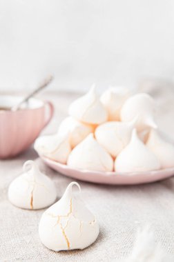 Ön planda çatlak ve desenli kremalı kurabiyeler. Arka planda, kremalar pembe bir tabakta yatıyor. Gri keten arka plan. Metin için yer.