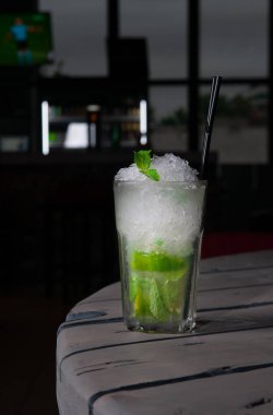 Mojito Long içeceği limonla süslenmiş ve nane şekeri ezilmiş buzla. Cam bir kadehte Collins. Gri ahşap bir arka planda. Yakın plan. Sert ışık