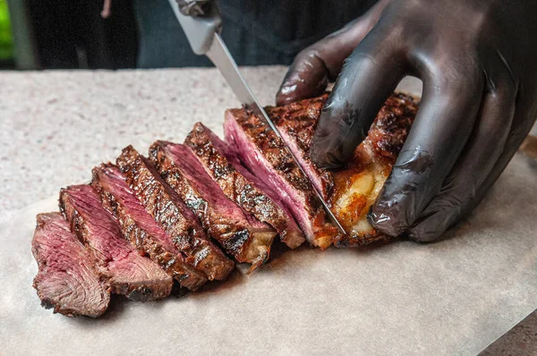 Medium Roast Beef Steak. Cut with a knife into pieces. Male hand in a black glove. Steak lies on parchment. Close-up.