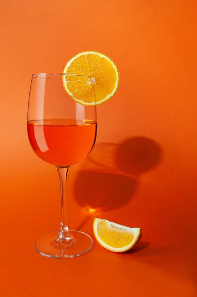 Cocktail aperol spritz. In a glass goblet. On a glass of orange slice. Next to the glass is a slice of orange. On a plain orange background. Hard light, sharp shadows. Close-up. Place for text.