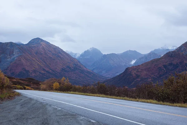Sonbahar Alaskan dağlarında bir yol. Bulutlar genel gider, mavimsi sabah ışık, kar dağlar, üst kısımları Center'da çift Sarı çizgi.