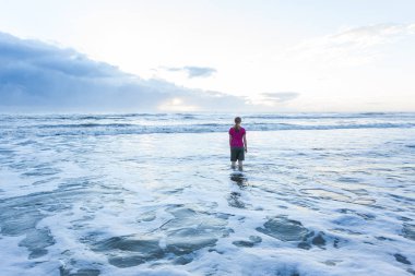 Genç Bayan şort ve tişört, sarı saçlı giyen Plajı'nda Okyanusu ayakta. Bu gündoğumu ve güneş ufukta gelmek başlıyor.