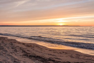 Michigan, kumlu bir plajda güneşin ufukta düşük ile çimen.