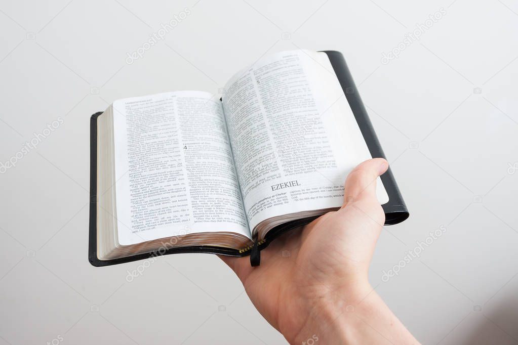 A small Bible open and held by a hand against a white background.