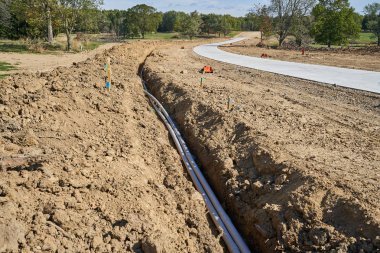 Yolun kenarındaki hendekte yeni bir PVC borusu var. Yeni bir konut inşaatı başladığından, beton yol yeni. Toprak birikmiş, boruları doldurmak ve kapamak için bekliyor..