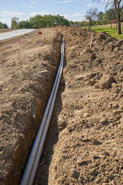 Yolun kenarındaki hendekte yeni bir PVC borusu var. Yeni bir konut inşaatı başladığından, beton yol yeni. Toprak birikmiş, boruları doldurmak ve kapamak için bekliyor..