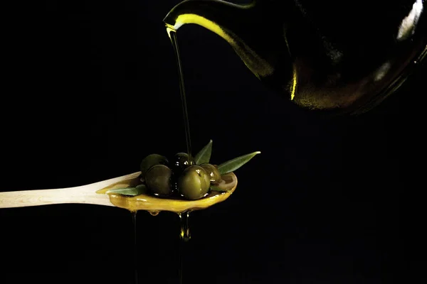 Aceite que cae sobre un puñado de aceitunas en cuchara de madera — Foto de Stock
