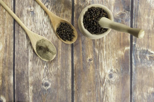 black peppercorns and ground black pepper on wooden spoons