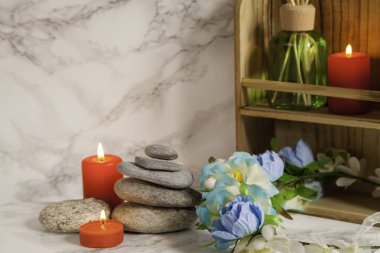Nehir çakıl taşları, kırmızı mumlar ve mermer üzerinde çiçekler, oda spreyi ve mermer zemin üzerinde mum olan ahşap raf.