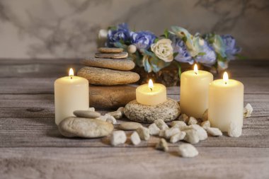 Nehir taşlarında dört mum, tahta masada çiçekler ve mermer arka planda.