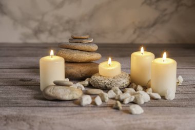 Ahşap masa ve mermer zemin üzerinde nehir çakıl taşları üzerinde dört mum.