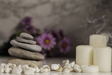 Dört tane yanmamış mum, dumanlı ve nehir çakıl taşlı mermer arka planda çözünmüş papatyalar.