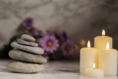 Nehir çakıl taşları ve mermer zemine odaklanmamış papatyaları olan dört mum.