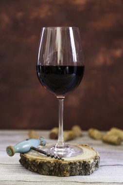 Tahta dilimlenmiş kırmızı şarap kadehi, eski tirbuşon ve ahşap masanın altında mantar ve kahverengi fantezi arka planı.