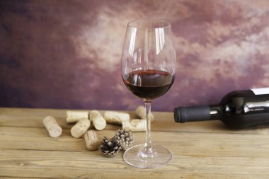 Bir bardak kırmızı şarap, mantar, kozalak ve şişe ahşap masa ve kahverengi fantezi arka plan