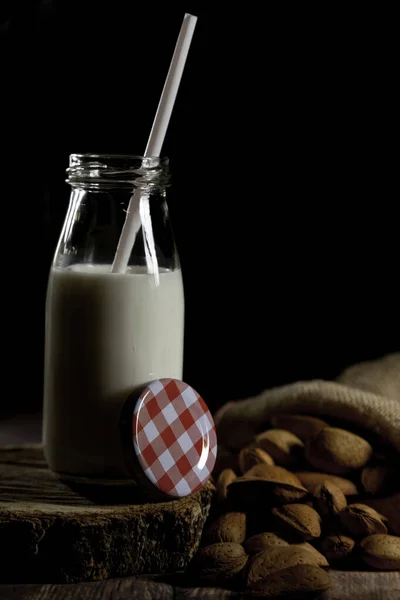 Homemade almond milk in a glass bottle and almonds sack on a wooden table and black backgroundl. The concept of healthy organic, farm products. Rustic style of still life. Copy space for text.