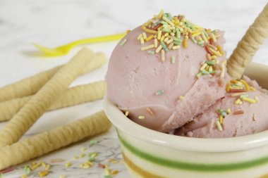 Seramik kasede iki çilekli dondurma, bisküvi yakından, sarı plastik çay kaşığı ve mermer arka planda çeşitli bisküviler. Boşluğu kopyala