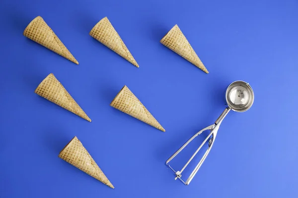 six of ice cream cone waffle in geometric formation and ice-cream spoon on blue background. Concept. Copy space