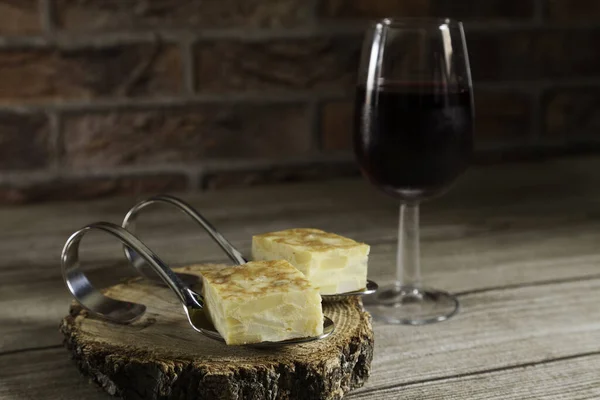 Spanish omelette brochettes on a wood slice and red wine glass on wooden table and red brick background