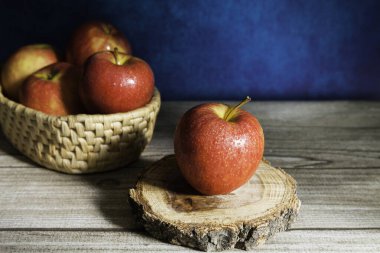 Ahşap dilimde lezzetli kırmızı elma ve ahşap masada sepet içinde elma grubu ve soyut mavi arkaplan
