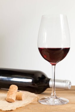 Kırmızı şarap şişesi uzanmış, kırmızı şarap kadehi ve mantarlar ahşap masada ve beyaz arka planda. Boşluğu kopyala