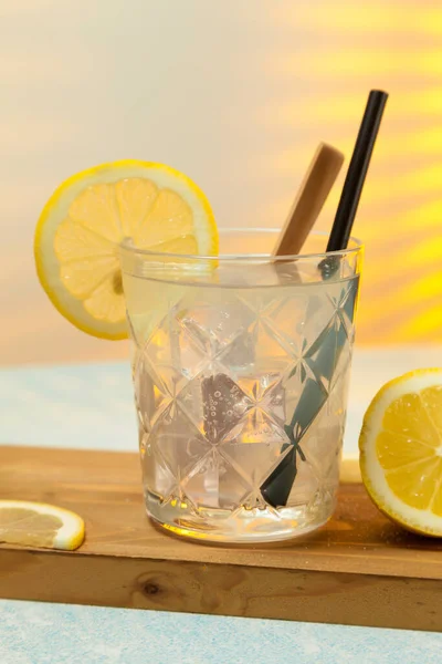 close-up of refreshing lemonade glass with ice, spoon and straw on cutting board on background with sunlight entering through rear window. Copy space