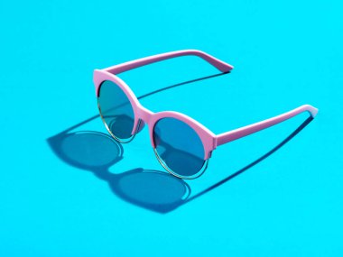 Pastel mavi arka planda pembe güneş gözlükleri