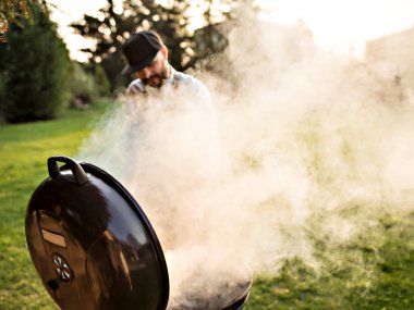 Genç sakallı adam dışarıda et pişiriyor..