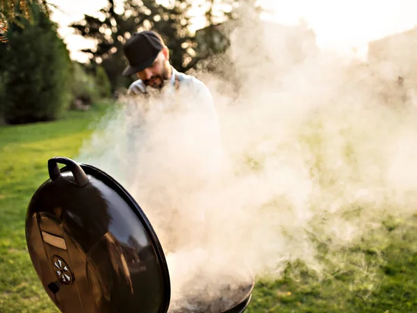 Młody brodaty człowiek gotuje mięso na świeżym powietrzu. — Zdjęcie stockowe