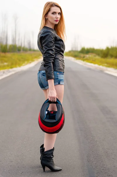 Schöne Radfahrerin steht mit Motorradhelm in der Hand auf der Straße — Stockfoto