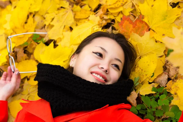 Sonriente chica coreana con gafas acostado en hojas — Foto de Stock