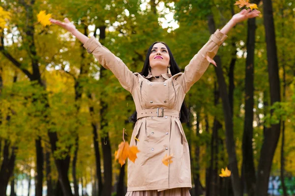 Счастливая брюнетка женщина бросает осенние листья вверх — стоковое фото