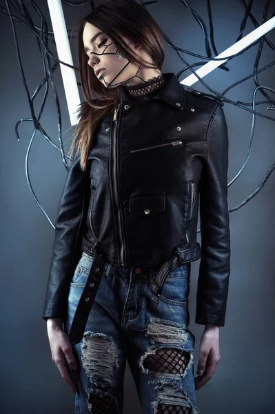 Элегантная девушка-робот в проводах в стиле киберпанк в кожаной куртке и разорванных джинсах — стоковое фото