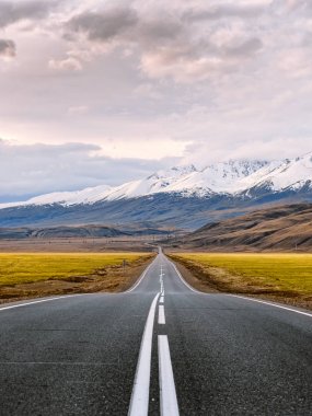 Dağlara giden yol davet. Düz asfalt yol ile beyaz yüzey işaretleri şapkalı kar dağlarda Altay Cumhuriyeti, Rusya gün batımına sadece geçer. İlham verici seyahat ve macera fotoğraf.