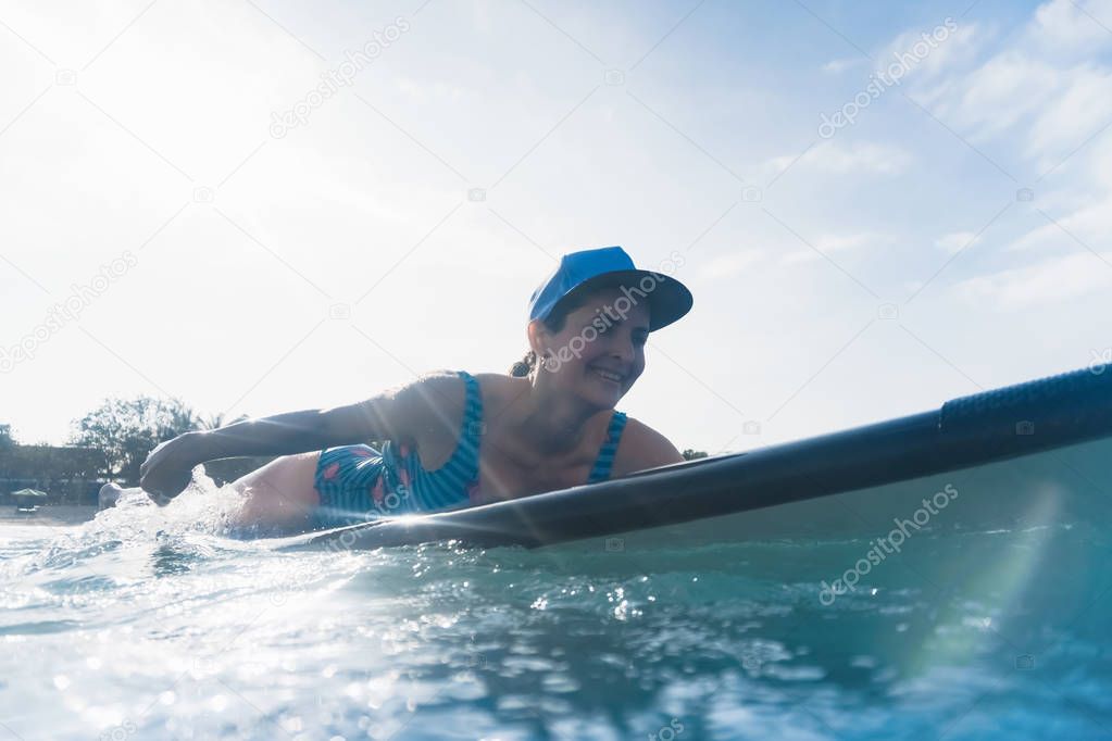 attractive smiling woman in cap lying on surfing board in ocean 