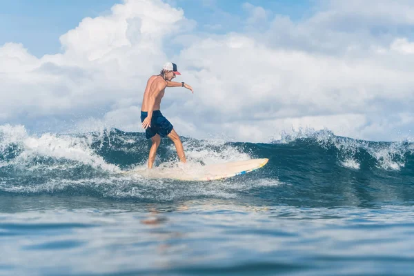 Man in swimming shorts and cap surfing in ocean — Stock Photo