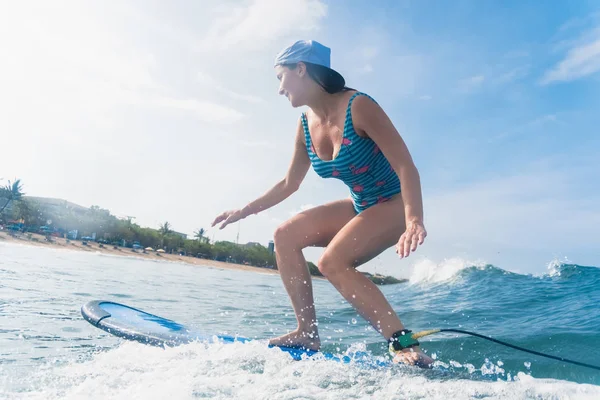 Side view of woman in cap and swimming suit surfing in ocean — Stock Photo