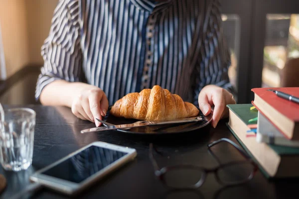 Woman eating croissant in cafe