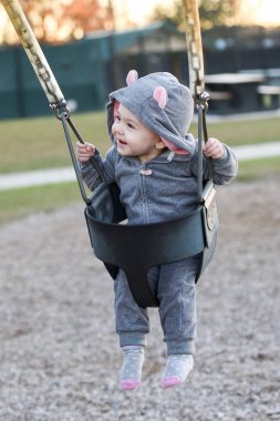 Fare hayvan kostümlü bir salıncak üzerinde çok mutlu küçük kız. Gülümseyen bir yaşındaki çocuk.