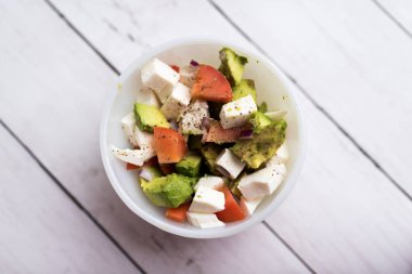 Avokado, domates ve beyaz kasede servis edilen taze mozzarella peynirli taze sebzelerden sağlıklı salata.